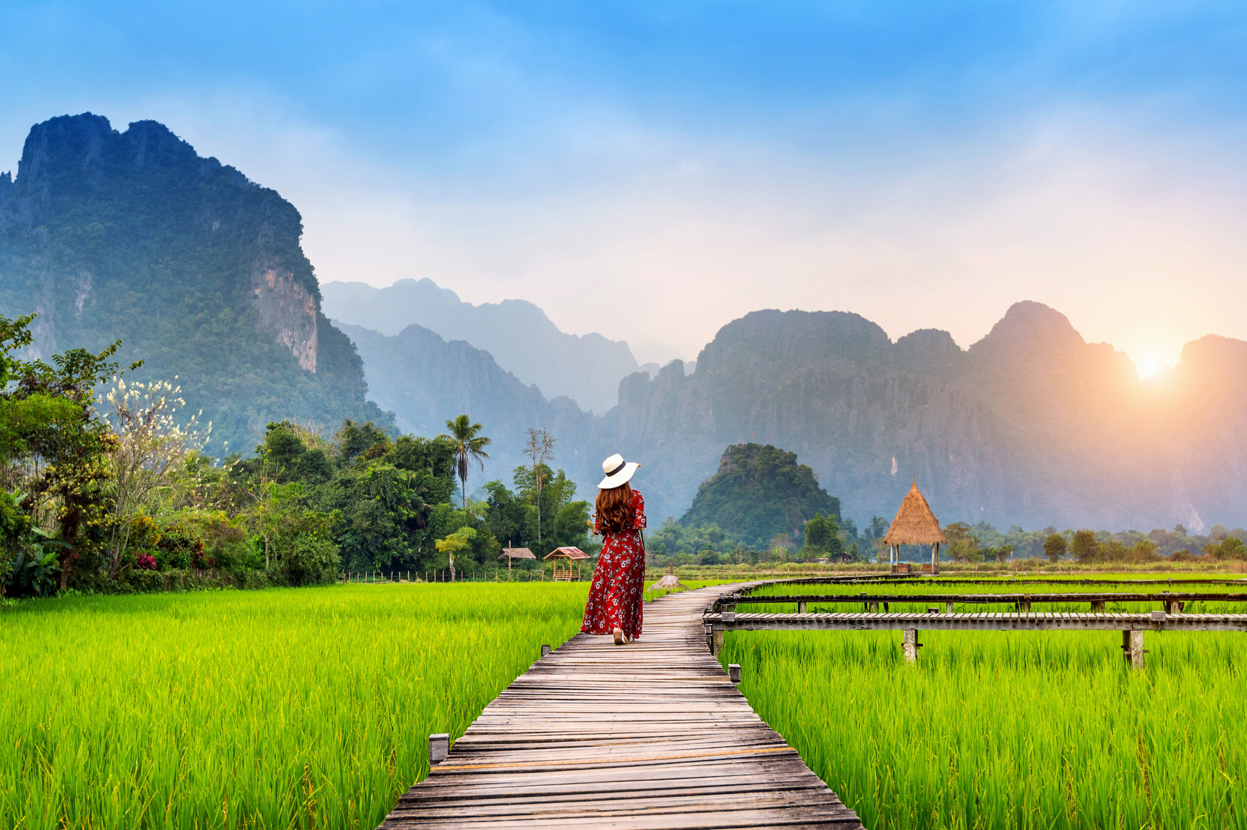 young-woman-walking-wooden-path-with-green-rice-field-vang-vieng-laos