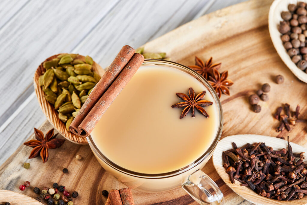 Traditional Indian drink - masala tea with spices. Cinnamon, cardamom, anise, sugar, cloves, pepper on a light wooden background.